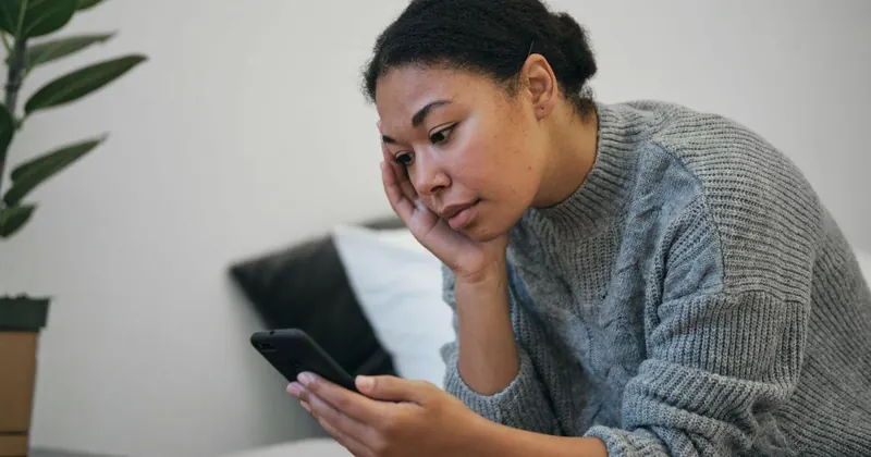 Mulher pensativa olhando para o celular, sentindo que precisa recomeçar