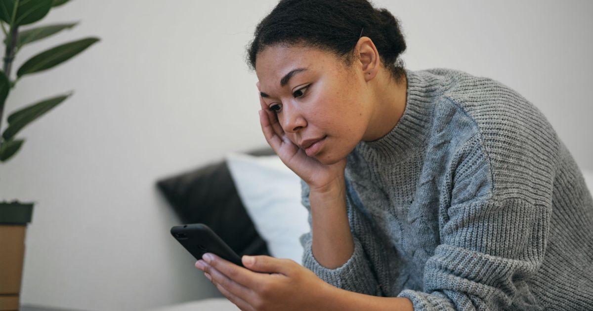 Mulher pensativa olhando para o celular, sentindo que precisa recomeçar