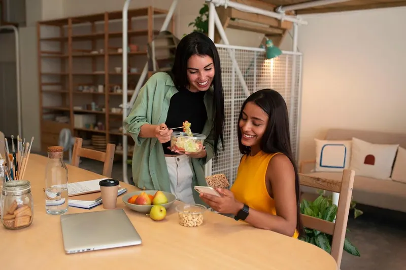 Duas amigas sorrindo enquanto compartilham refeição saudável